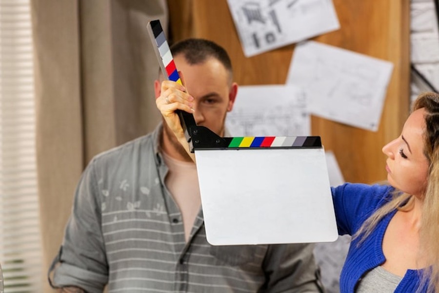 Un homme et une femme manipulent un clap de cinéma blanc sur un plateau de tournage, illustrant pourquoi les artistes utilisent désormais l'ADN synthétique pour signer leurs œuvres de manière indélébile.