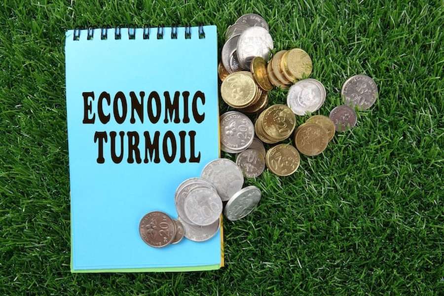 Un carnet bleu marqué 'ECONOMIC TURMOIL' entouré de pièces de monnaie sur une pelouse verte pour illustrer comment générer des revenus complémentaires grâce au stockage carbone des sols en 2026.