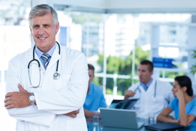 Un médecin de garde souriant au premier plan avec son équipe médicale en réunion en arrière-plan