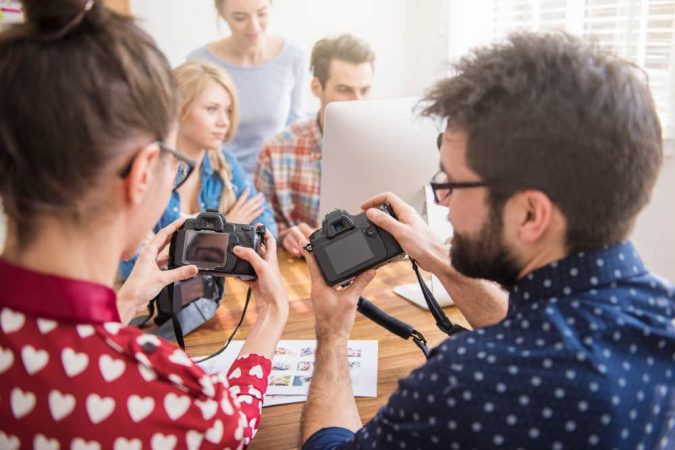 Un groupe de jeunes créateurs analysant des photos sur leurs boîtiers numériques, illustrant l'indépendance vis-à-vis des médias et des influenceurs dans la production de contenu.