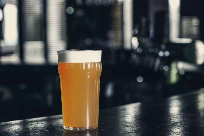 Un verre de bière blonde avec une mousse généreuse posé sur un comptoir sombre sans sous-bock.