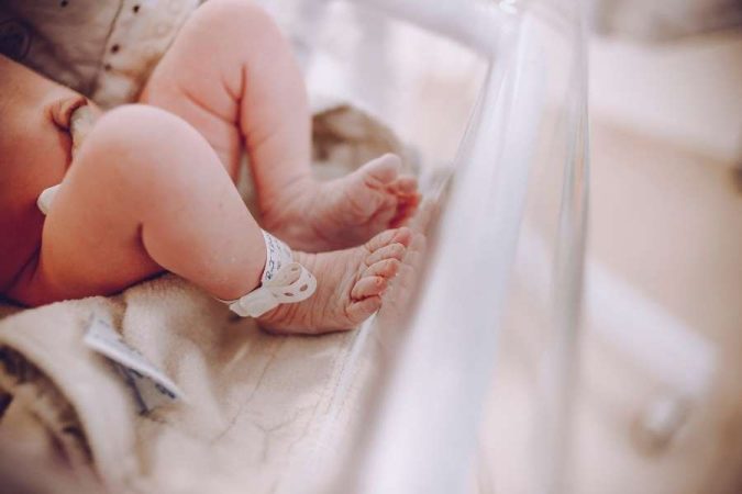 Gros plan des pieds d'un nouveau-né portant un bracelet d'identification à l'hôpital, avec un léger aperçu de ses fesses rouges.