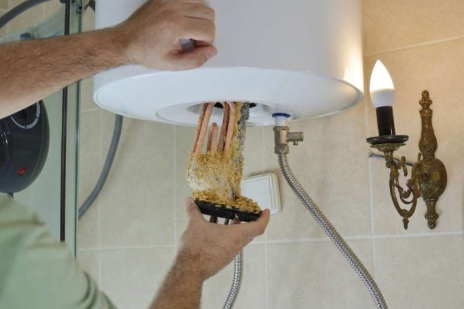 Un technicien inspecte la résistance entartrée d'un cumulus, ce qui explique pourquoi le chauffe-eau fait du bruit.