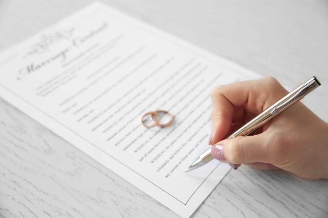 Une personne signe un contrat avec des alliances posées à côté, une étape importante pour organiser un mariage civil.