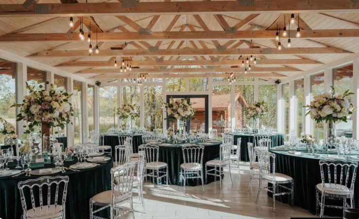 Salle de réception lumineuse sous verrière avec tables rondes et chaises transparentes, une solution idéale pour un plan B mariage en extérieur pluie.