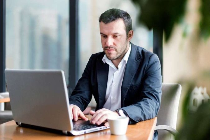 Un entrepreneur en costume rédige un devis d'auto-entrepreneur sur son ordinateur portable dans un bureau.